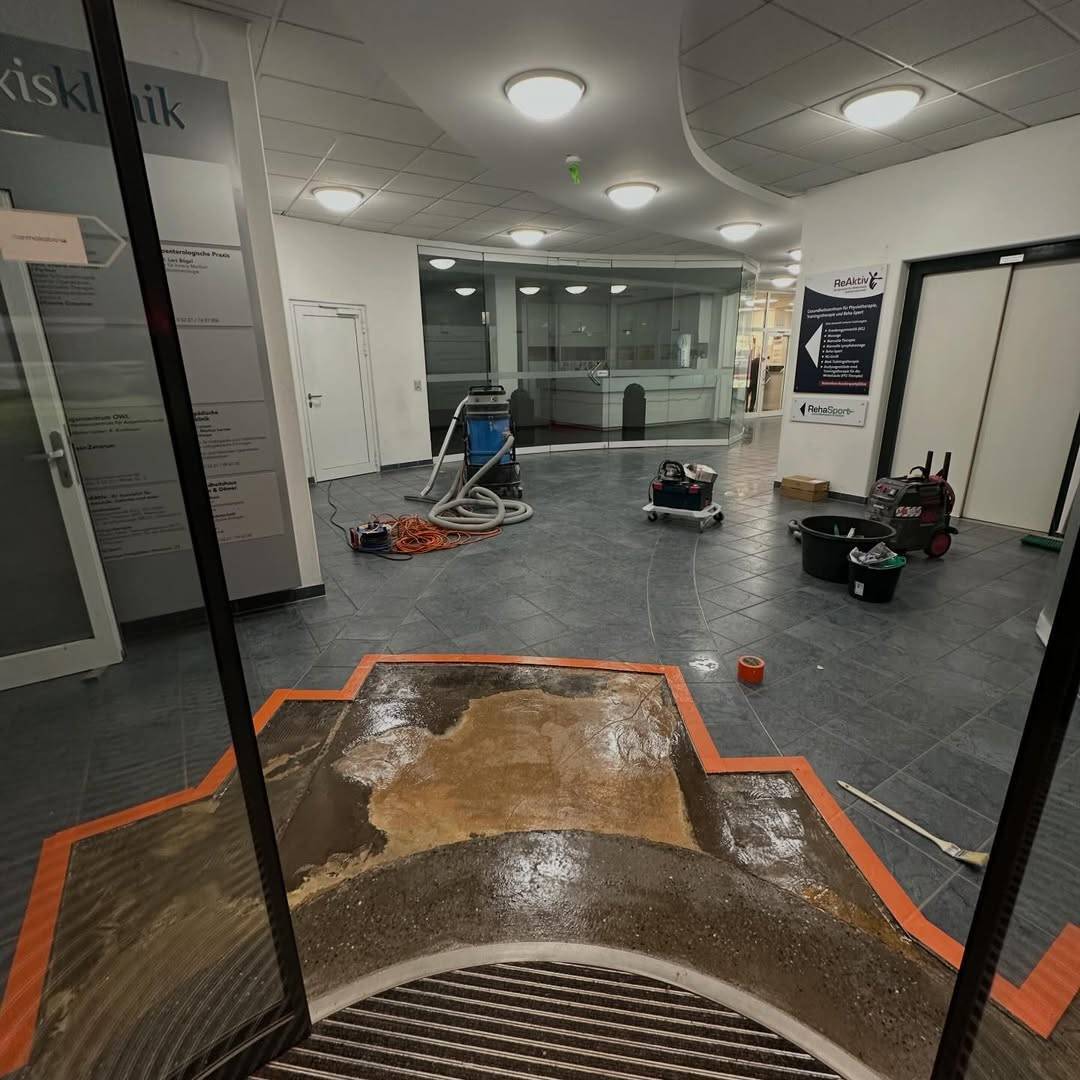Dunkelgrauer Boden in einem Eingangsbereich bei der Vorbereitung, orange abgeklebte Fläche und Industriesauger
